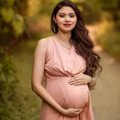 A classic and graceful portrait of a mother-to-be in a flowing pink gown. The soft, blurred greenery of the natural background puts all the focus on her serene expression and the life she is carrying.