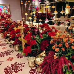 A vibrant tablescape for a traditional celebration. The table runner is a dense arrangement of red and orange florals, accented with brass bells and set upon a custom block-printed tablecloth.