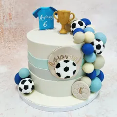 We score a goal with this stylish football champion cake. A personalized jersey, a golden trophy, and a cascade of footballs and spheres in team colors adorn this modern cake, making it the perfect centerpiece for a football fan's birthday.
