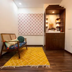 A cozy and traditional prayer corner featuring a wooden pooja mandir with storage. The vibrant yellow rug and comfortable seating create a warm and inviting space for daily devotion.