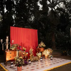 The full view of the reception stage featuring an upcycled red dupatta as a vibrant backdrop. The setup includes a floor covering, antique furniture, and floral arrangements, creating a complete and personalized photo corner.