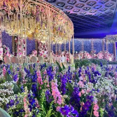 A garden of earthly delights. This reception stage is a floral masterpiece, with a structure completely enveloped in a sea of purple, pink, and white flowers, set against a sparkling backdrop.