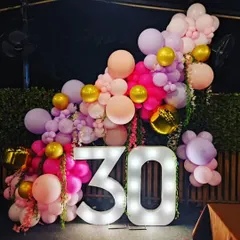 A beautiful outdoor balloon arrangement for a 30th birthday. The organic garland in shades of pink and lilac, accented with gold balloons, creates a soft and celebratory frame around the large marquee numbers.