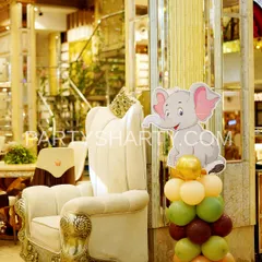 A cute elephant character prop on a balloon column, placed next to a regal throne chair for the birthday child in a jungle-themed party.