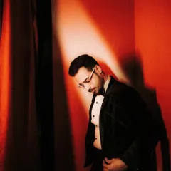 A dramatic and stylish portrait of the groom. The strong red light and shadows create a moody, cinematic feel, highlighting his sharp attire and pensive look.