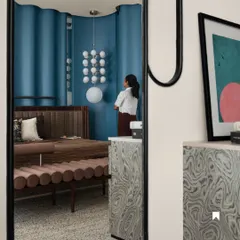 A reflection in the custom mirror shows the layers of design in the master bedroom. The blue ripple wall, the plush upholstered bench, and the statement lighting all come together to create a space that is rich in texture and personality.