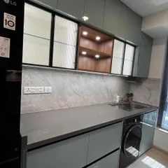 A combination of fluted glass and open wooden shelving provides both concealed and display storage. The warm light from the open shelf contrasts beautifully with the cool tones of the grey cabinets and marble-patterned backsplash.