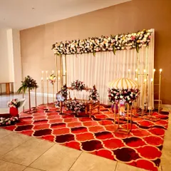 An elegant naming ceremony setup for little Adhokshaj. The stage features a beautiful floral arrangement on a gold frame, a decorated cradle (jhoola), and traditional lighting elements.