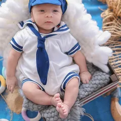 A close-up portrait of the baby in his adorable sailor costume, showing the details of his outfit and his calm, observant expression.