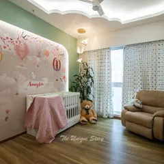 This nursery is a cozy and safe haven, featuring a white crib set against the whimsical mural. A comfortable recliner provides a perfect spot for feeding and bedtime stories, while the cloud-shaped false ceiling adds a touch of magic.