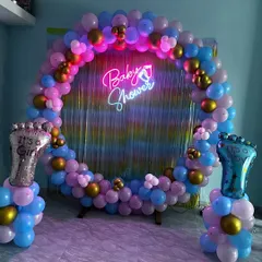 A "He or She" themed baby shower ring in pink, blue, and gold, with a "Baby Shower" neon sign and an iridescent backdrop.