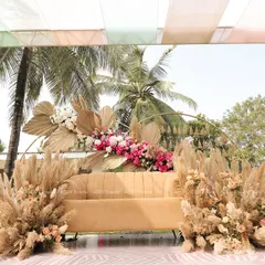 For a sun-drenched Mehndi ceremony, we designed this stunning boho-chic seating area. The arrangement features a comfortable lounge sofa framed by an arc of dried palm leaves, pampas grass, and vibrant pink florals, creating a picture-perfect spot for the couple.