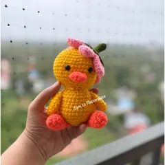 This cheerful little duck is wearing a flower on its head. It's a small, cute toy that is perfect as a gift or party favor.