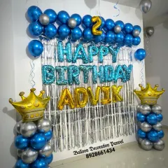 A handsome blue and silver birthday decoration for a 2nd birthday. The setup features balloon pillars topped with crowns and a silver foil curtain.