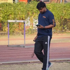 At my workspace, the track. Checking my phone to review a recorded video of an athlete's drill to analyze their technique in detail.