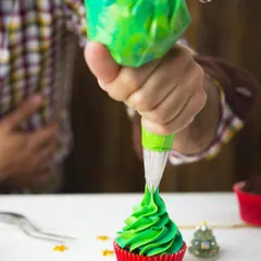 A participant at our cupcake workshop piping a perfect green swirl of frosting. I'll teach you the techniques to make your cupcakes look professional.