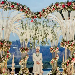 The groom stands proudly at the mandap, awaiting his bride. The stunning floral decor and scenic backdrop make this a truly grand portrait.
