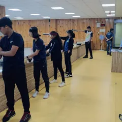Students practice their 10-meter pistol shooting stances in a line. This image captures a typical training day where shooters work on consistency and aim under supervision.