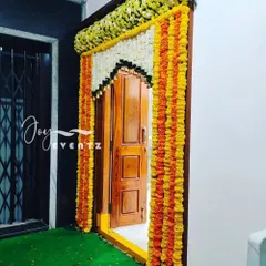 A traditional housewarming door decoration using garlands of orange and yellow marigolds and white jasmine. This classic design brings a festive and auspicious feel to your new home's entrance.