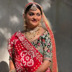 A beautiful Gujarati bride in a traditional red bandhani saree. The makeup is kept classic and radiant to complement the vibrant colors and heavy embroidery of her outfit.