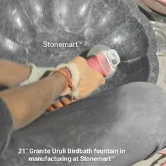 An artisan is polishing the inside of a 21-inch granite uruli birdbath. This finishing process ensures a smooth surface and brings out the stone's natural luster.