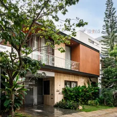 The completed Prakash Reddy residence, surrounded by lush landscaping. The design uses a mix of travertine marble and wood-finish cladding to create a warm, modern, and inviting exterior.