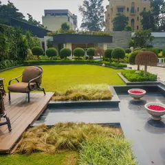 This residential garden is a perfect example of integrated landscape design. A sleek water feature is bordered by a wooden deck, ornamental grasses, and a manicured lawn, with carefully sculpted trees in the background, creating a space with diverse textures and zones.