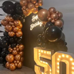 This view highlights the full curve of the balloon arch as it frames the backdrop. The mix of different sized balloons in metallic bronze and classic black adds texture and a modern, sophisticated feel.