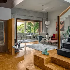Bold choices can define a home. The vibrant turmeric-yellow oxide flooring brings immense warmth to this space, beautifully contrasting with the cool grey tones and connecting the multi-level living areas to the lush green balcony outside.