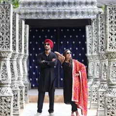 A modern and stylish portrait of a couple in matching black ethnic wear. Their confident poses and sunglasses give a cool, editorial vibe to this shot taken among carved pillars.