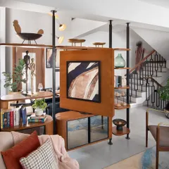 This custom partition is the heart of an open-plan living area, solving the need for both separation and connection. The central panel, featuring a rotating television, allows for viewing from either the living or dining space, while the open shelving maintains a sense of light and airiness.
