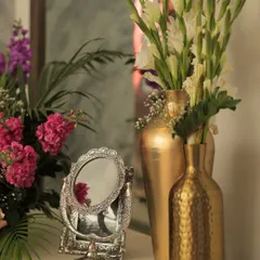 A touch of vintage charm. This small decor vignette combines a silver vanity mirror with fresh flowers in hammered gold vases, adding a touch of elegance to a corner space.