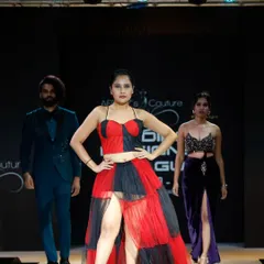 Three models on the runway at the IDL show, presenting a red and black tiered gown, a men's green suit, and a purple velvet two-piece.