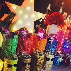 A collection of colorful tiki-style mugs and other retro decor. The glowing star marquee and vibrant flowers add to the fun, nostalgic feel of this 80s-themed cocktail bar.