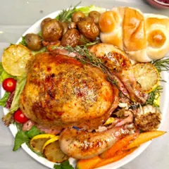 Our Easter feast centerpiece: a succulent whole roasted chicken stuffed with vegetables and herbs, served with sausages, roasted potatoes, and fresh bread rolls. A complete and celebratory meal.