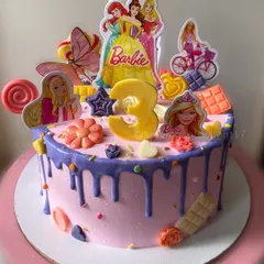 A dream cake for a Barbie fan turning three. This pink drip cake is loaded with Barbie characters, lollipops, and chocolate bars for a fun and festive look.