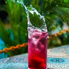 A dynamic action shot capturing the perfect splash in a vibrant red cocktail against a lush green background. This kind of high-speed beverage photography is ideal for creating exciting visuals for bar menus and social media campaigns.