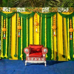 A simple and traditional stage backdrop suitable for a Haldi or Mehandi ceremony. It uses yellow and green drapes with hanging marigold decorations for a festive look.