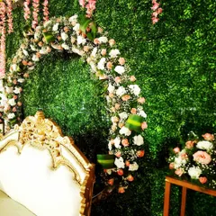 A side angle of the engagement backdrop, highlighting the texture of the floral arch against the green wall. The details in the flowers and the ornate sofa are clearly visible.