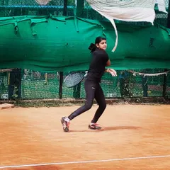 A junior girl hits a focused backhand during an AITA U-14 tournament match, demonstrating proper form and concentration.