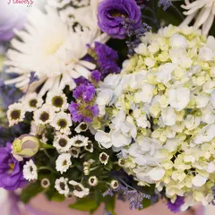 A close-up view highlighting the delicate textures of the flowers. You can see the soft petals of the hydrangea, the intricate layers of the eustoma, and the fresh white chrysanthemums that complete the bouquet.