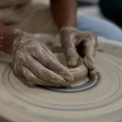 Getting your hands muddy is part of the fun. Here, a student is learning to center the clay, which is the most important skill for wheel throwing.