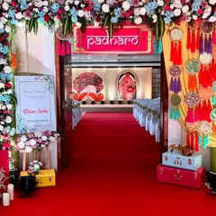 A vibrant and festive entrance for a 'Raas Leela' themed event. A bright red carpet leads guests through a floral archway towards a stage with traditional motifs.