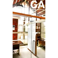 Inside a climate-responsive office in Bangalore. The combination of exposed brick walls, a high ceiling with a visible roof structure, and glass partitions allows light to travel deep into the space, creating a bright and open work atmosphere.