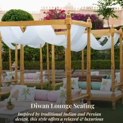 A luxurious Diwan lounge seating arrangement for an outdoor event. The wooden four-poster daybeds with white drapes and palm-printed cushions offer a relaxed yet regal vibe, inspired by traditional Indian design.