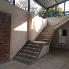 During construction at an artist's farm, a sharp diagonal of sunlight cuts across a lime-plastered wall, highlighting the texture of the material and the raw geometry of the concrete staircase.