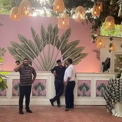A custom-designed photo wall for a tropical-themed Mehendi. The hand-painted pink backdrop with large banana leaves adds a fun, artistic, and highly photogenic element to the event decor.