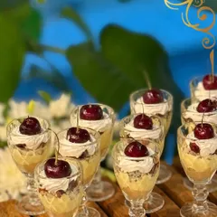 Layers of indulgence in a glass. This mini trifle dessert features cake, cream, and fruit, all crowned with a fresh cherry for an elegant and classic sweet treat.