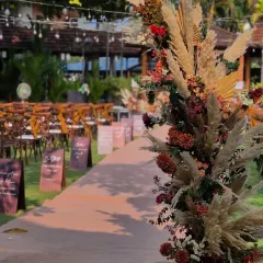 A close-up of the aisle entrance decor. The arrangement combines fluffy pampas grass with deep red and orange florals, establishing the rustic and warm color palette for the entire event.