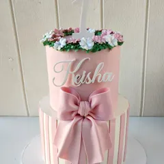 A dreamy two-tiered cake for a first birthday. The design features a pink and white striped bottom tier with a large bow, and a pink top tier with a floral crown and the number '1'.